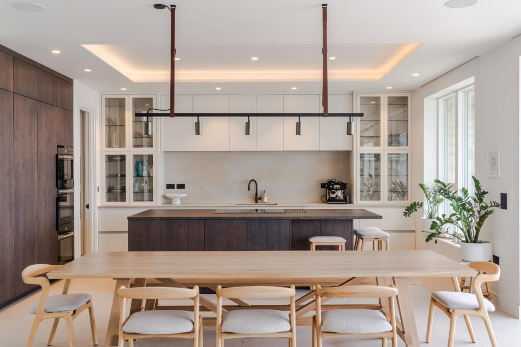 Dining table and chairs in front of a fitted kitchen with dark timber island at Bexhill-on-Sea