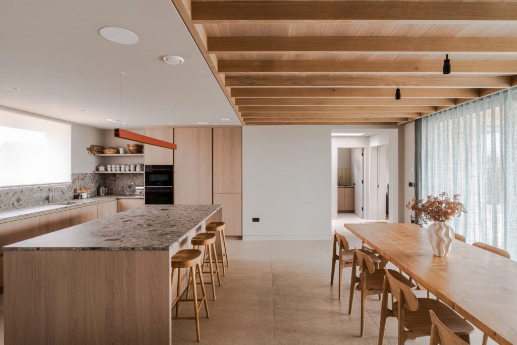 Open-plan kitchen and dining room with a stone-topped island and timber ceiling beams at Camber Sands