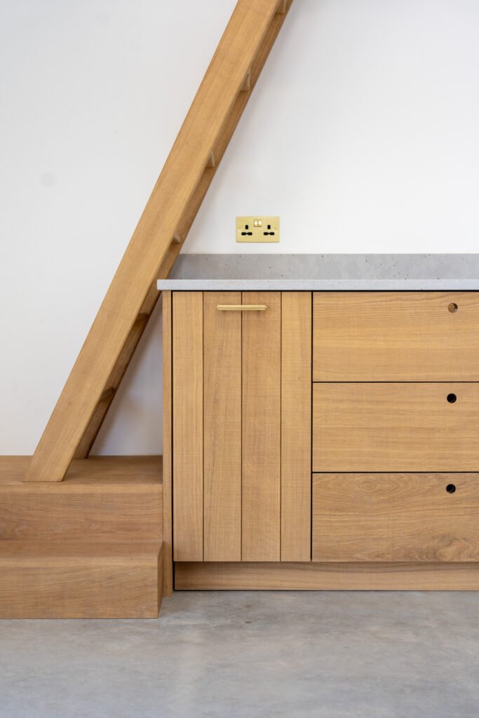 Oak kitchen cupboards and drawers beside a timber staircase at Camber Sands Pool House