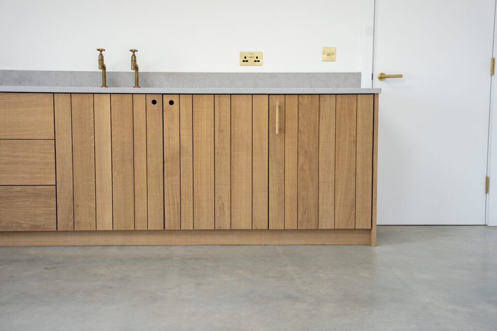 Textured oak kitchen base cabinets beneath a grey worktop and brass tap at Camber Sands Pool House
